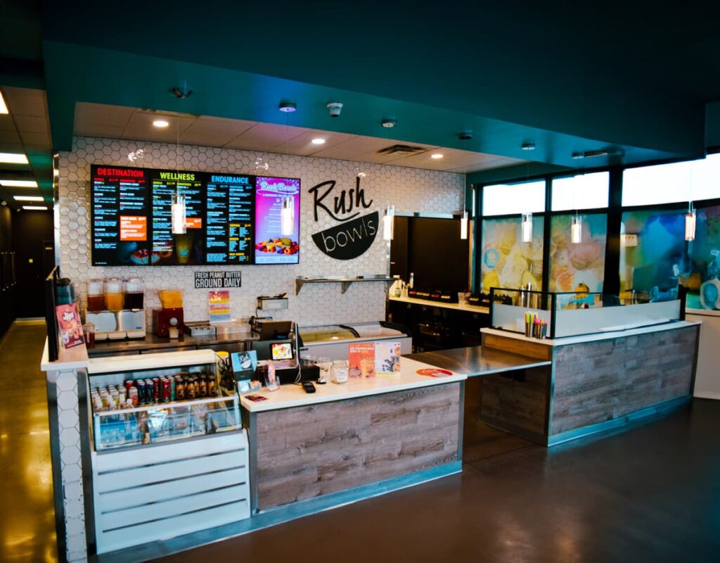 The interior of the smoothie and acai bowl shop reflects sleek commercial construction with its modern design. The counter showcases various toppings, while a digital menu board lists options under categories like Destination and Wellness. Bright, inviting lighting complements the clean layout.